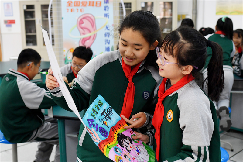 兩名學(xué)生在交流“愛耳護(hù)耳”彩繪海報(bào)。