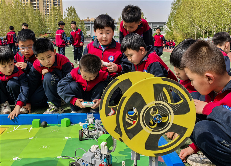 2025年4月16日，山東省樂陵市市中街道阜平小學(xué)科技勞動周現(xiàn)場，小學(xué)生在通過無線指令遙控“機(jī)器人”做游戲。