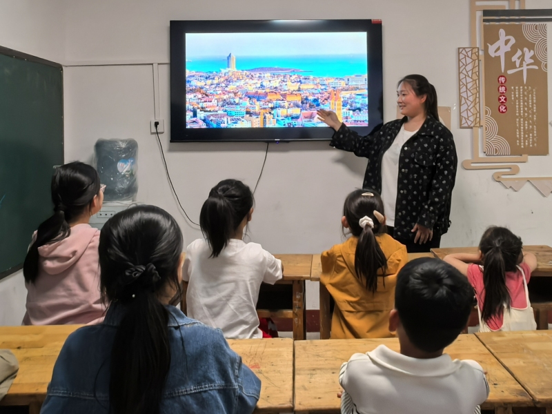 門莊村大學(xué)生志愿者參與讀書會(huì)，給孩子們講故事“山外的世界——青島”。沂水縣委宣傳部供圖