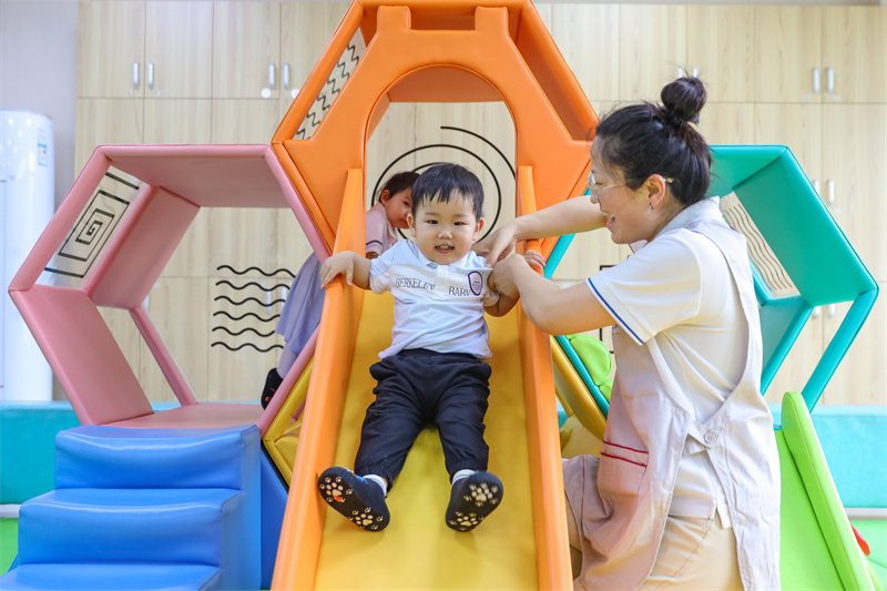 2025年5月14日，在山東省青島市李滄區(qū)職工子女愛(ài)心托育中心，小朋友在老師的陪伴下玩滑梯。張鷹 攝