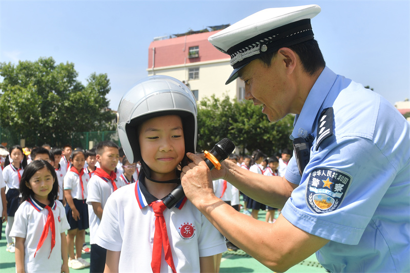 2025年7月4日，在山東省青島市市北區(qū)東勝路小學(xué)暑期休業(yè)式上，交警在指導(dǎo)學(xué)生正確佩戴安全頭盔。王海濱攝