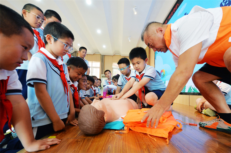 2025年7月4日，在山東省青島市市北區(qū)宜陽路小學(xué)暑期休業(yè)式上，救生協(xié)會志愿者在指導(dǎo)學(xué)生學(xué)習(xí)心肺復(fù)蘇技能。王海濱攝